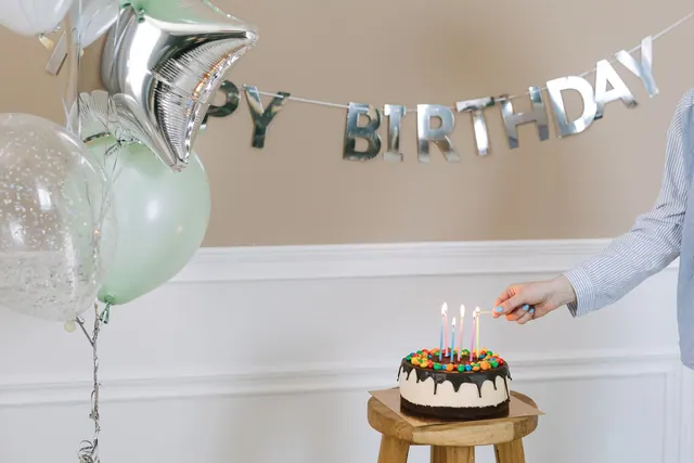 Bright birthday setup featuring a cake with candles, balloons, and a happy birthday banner. April birthdays by day: notable people organized by date