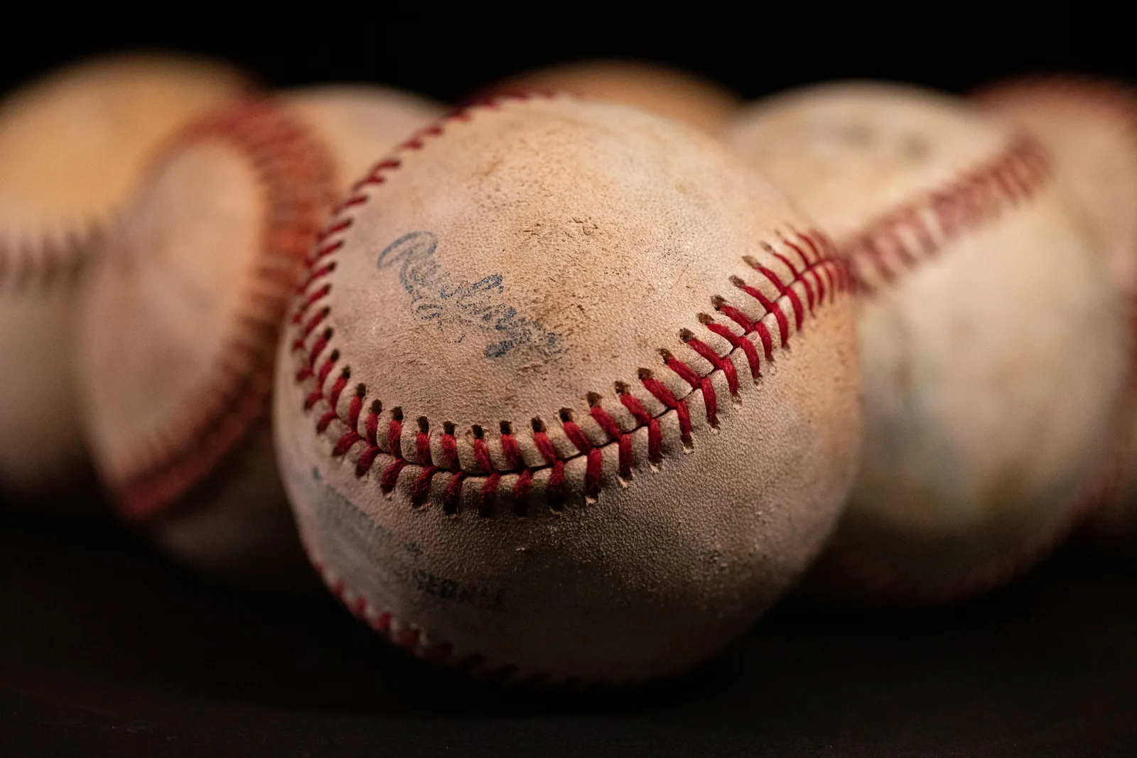 Focused close-up of old baseballs with visible stitching and texture against a dark background. The role of US sports leagues in publishing athlete birth dates