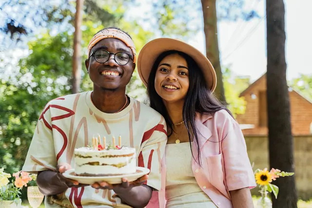 Two adults celebrating a birthday outdoors with a cake adorned with candles, smiling and happy. August birthdays: facts, records and changes