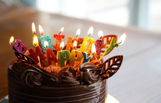Close-up of a chocolate birthday cake with colorful, glittering candles spelling 'Happy Birthday'. June birthdays: organized lists and source notes