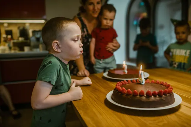 Young boy celebrating birthday by blowing candles on chocolate cake with raspberries. May birthdays: how to search and verify records